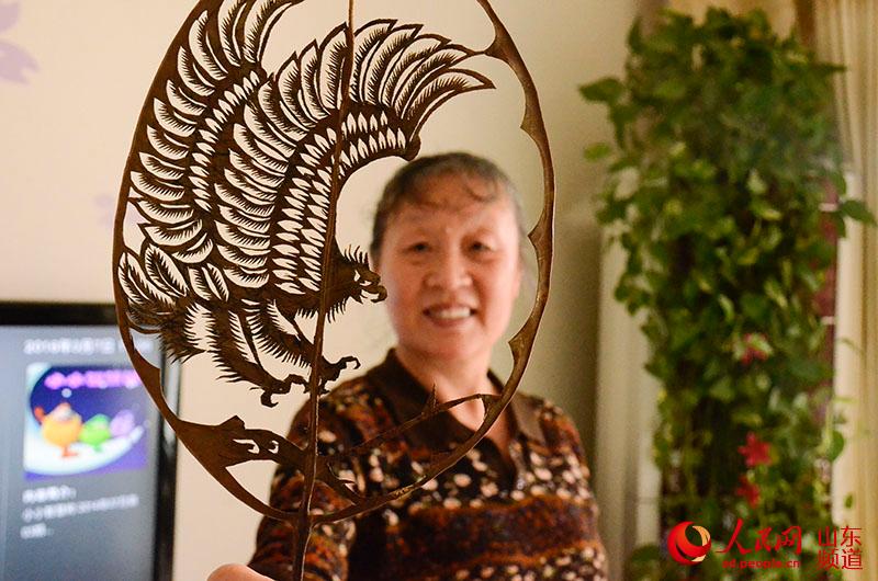 都婉莉在展示她的叶雕作品，山东61岁的都婉莉是一位剪纸和叶雕艺术家，“冷峻的苍鹰”在她的手里变得有了生命力。陈心同 摄